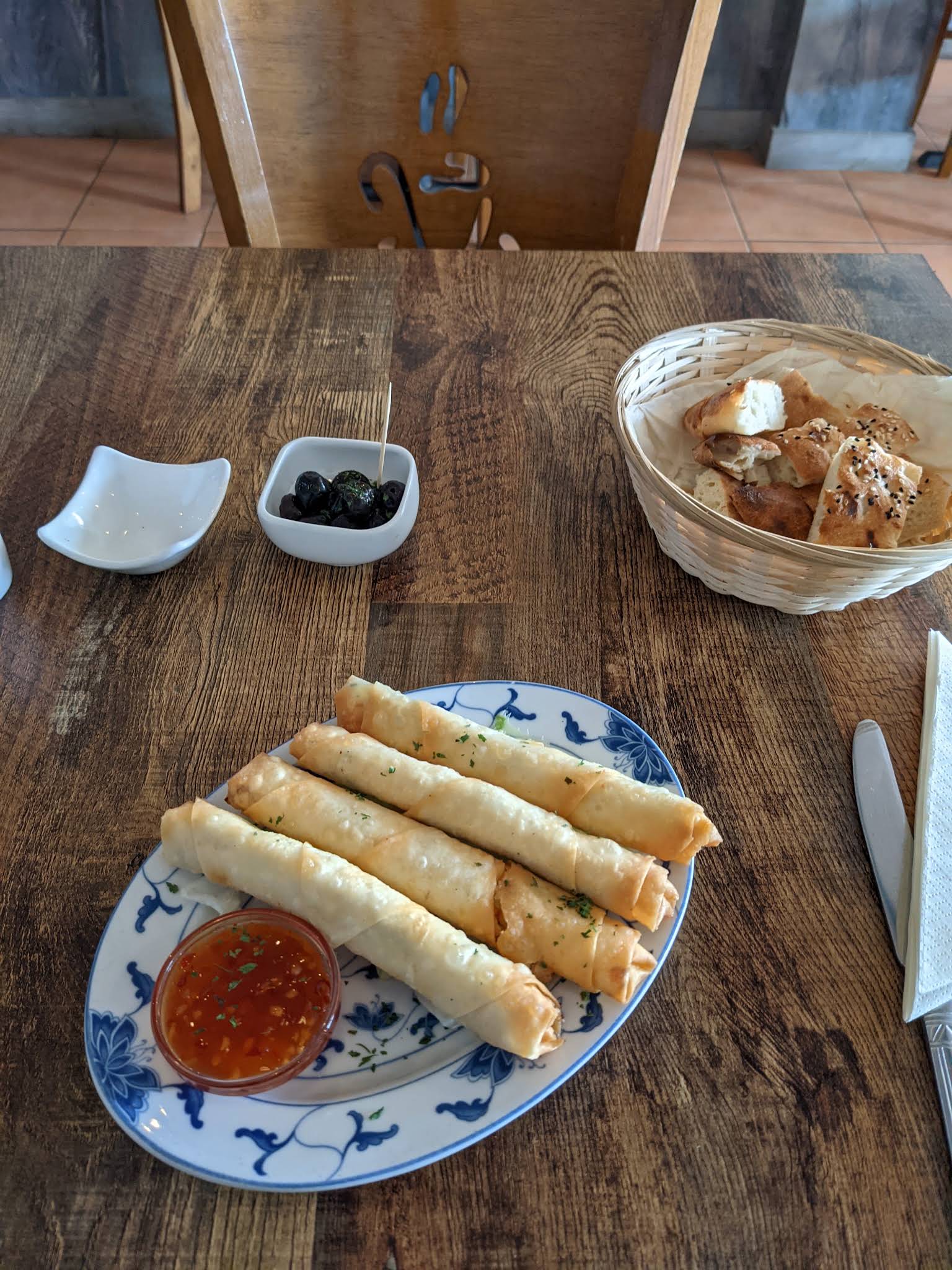 A complete blue and white plate of golden pastry rolls with a red dipping sauce on a wooden Lamarina table